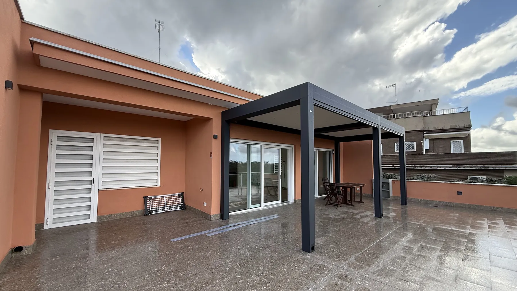 Terrazzo con una pergola scura, una grata bianca e una portafinestra scorrevole