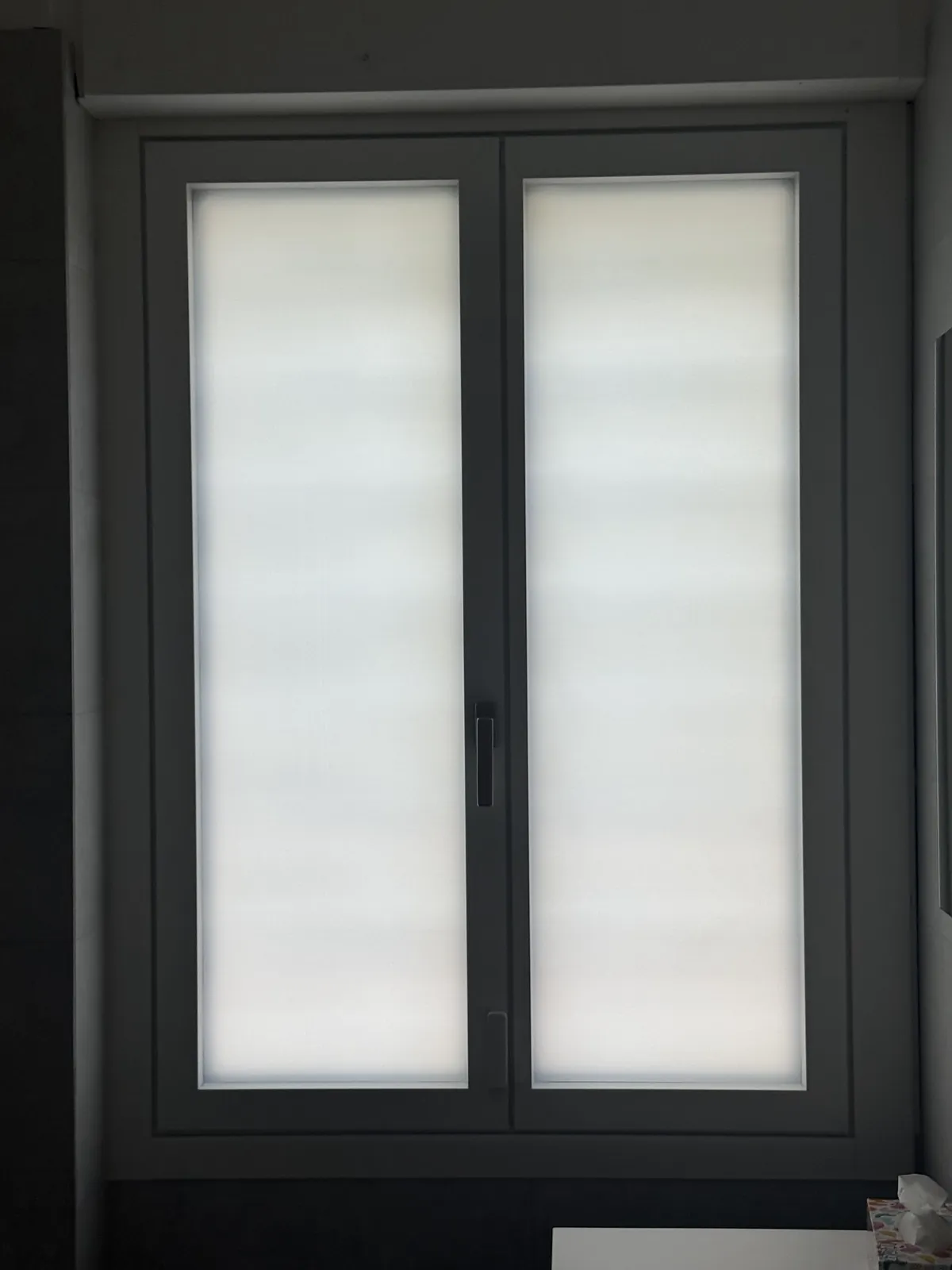 Finestra nuova a due ante con il telaio grigio scuro e le tende a rullo chiuse, vista dall’interno