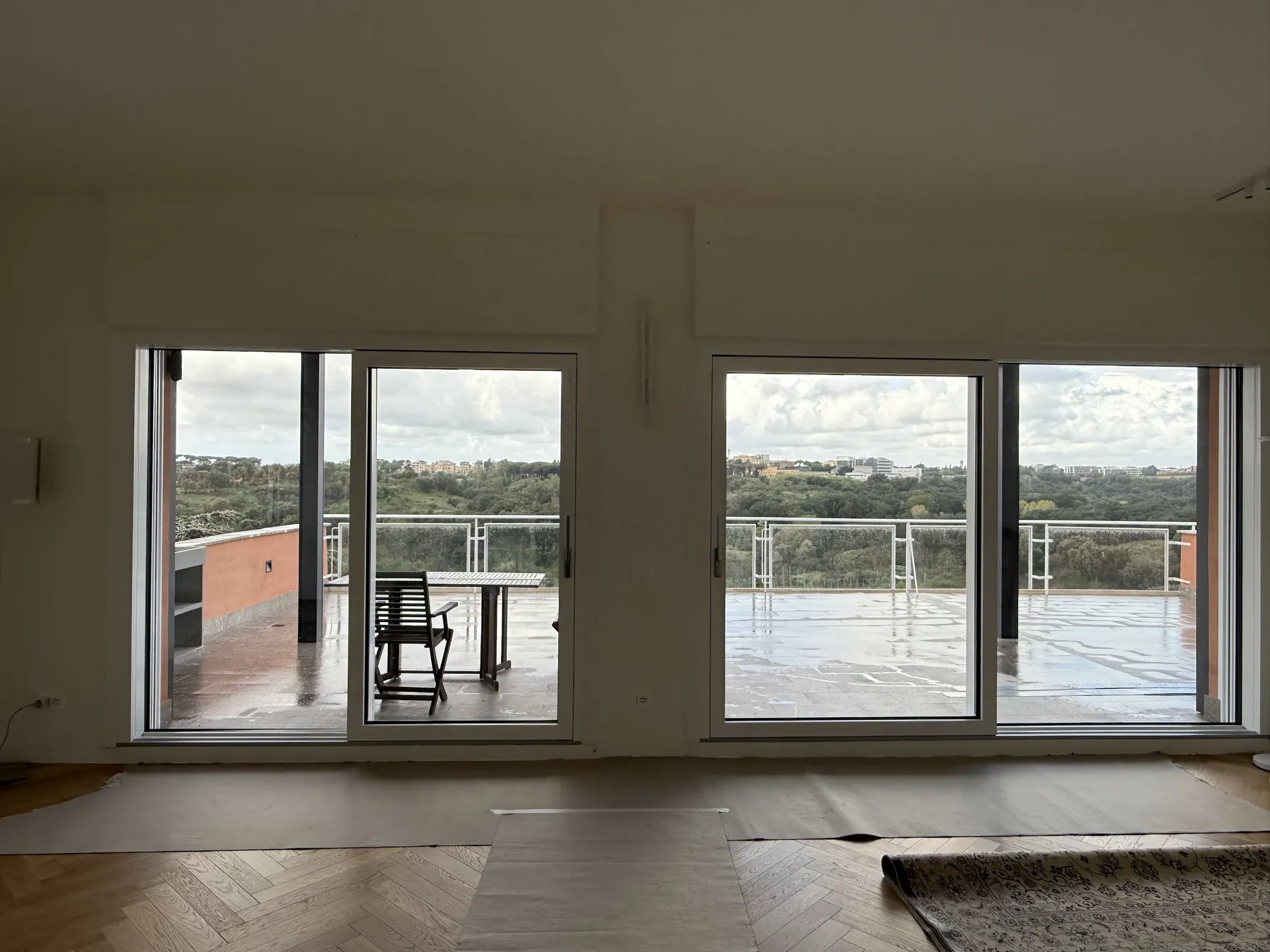 Soggiorno vuoto con due portefinestre nuove a tutta altezza che si aprono su una grande terrazza con vista sul verde