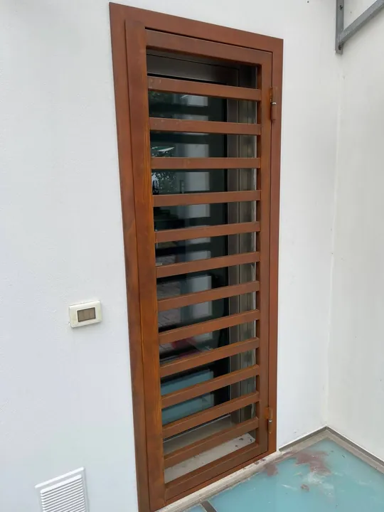 Grata color ruggine a tutta altezza davanti a una porta d’ingresso, su un muro bianco