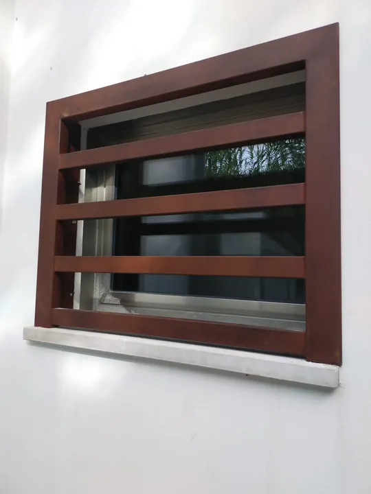 Grata fissa color ruggine a barre orizzontali su una finestra, muro bianco
