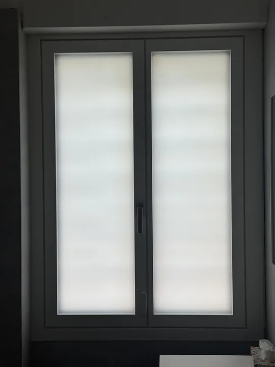 Portafinestra nuova con il telaio grigio scuro e le tende a rullo, vista dall’interno